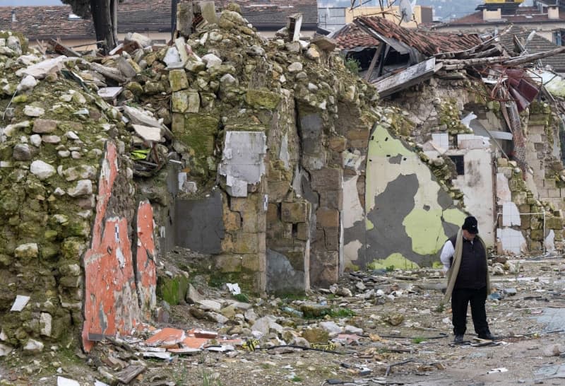 A man stands in front of destroyed houses in the old town of Antakya. Numerous houses in the city center were destroyed or severely damaged in the quake a year ago. Boris Roessler/dpa