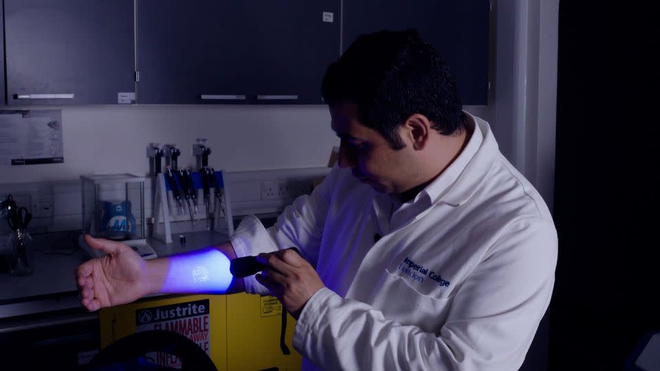 At his Imperial College London lab, Ali Yetisen demonstrates a stamp on his arm created using tattoo ink that glows under certain light. - CNN