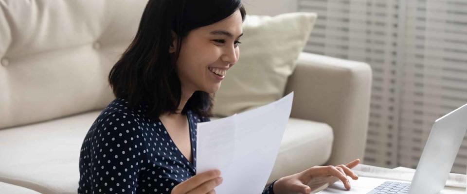 Close up smiling Asian woman checking financial documents, using laptop