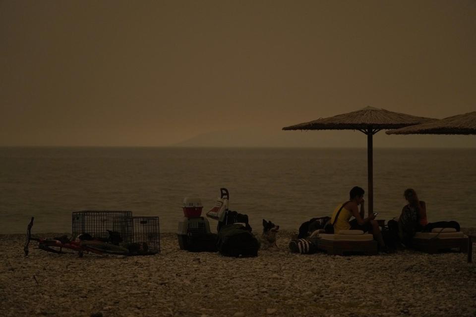 People with their pets gather on the beach during a wildfire at Pefki village on Evia island, about 189 kilometers (118 miles) north of Athens, Greece, Sunday, Aug. 8, 2021. Pillars of billowing smoke and ash are blocking out the sun above Greece's second-largest island as a days-old wildfire devours more pristine forests and triggers more evacuation alerts. (AP Photo/Petros Karadjias)