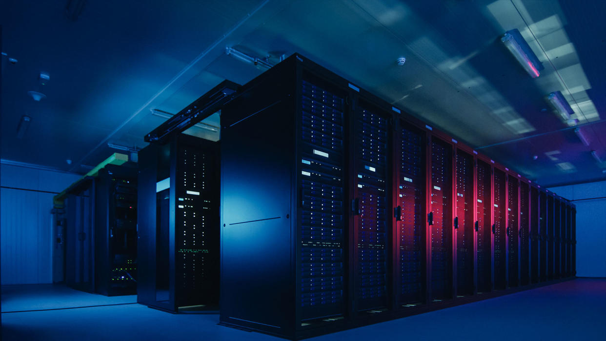  Data center with major computer processors with blue and pink lights in a dark room. 