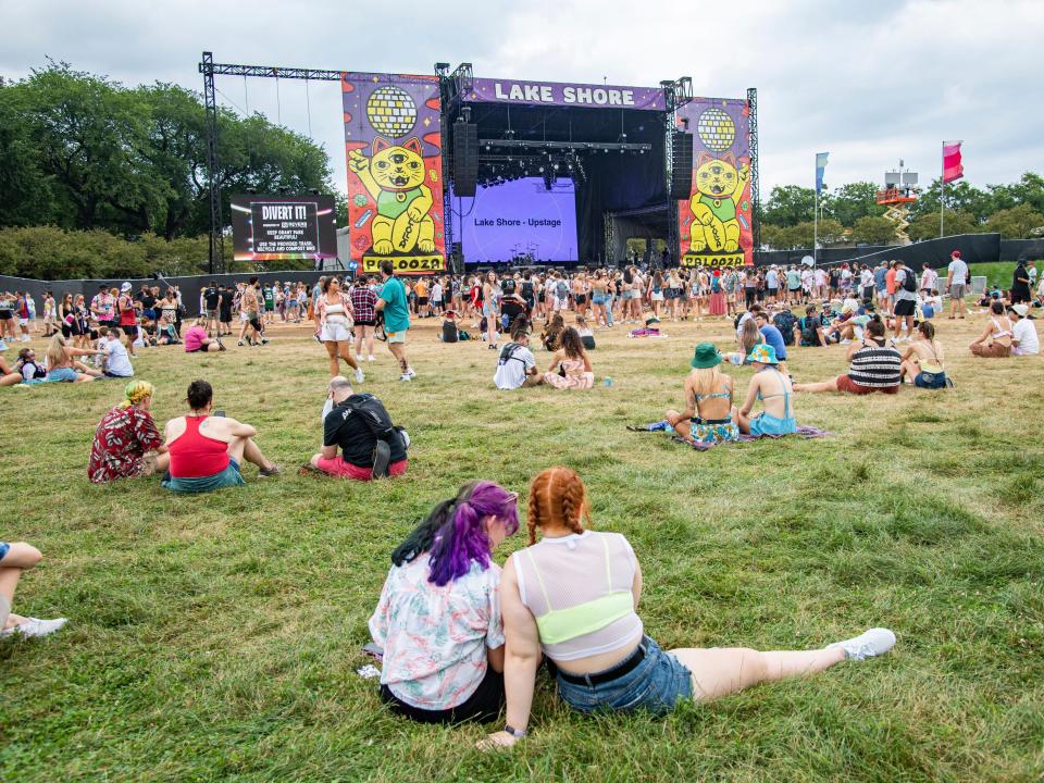 Festival goers sit on grass in front of Lake Shore stage at Lollapalooza Music Festival.