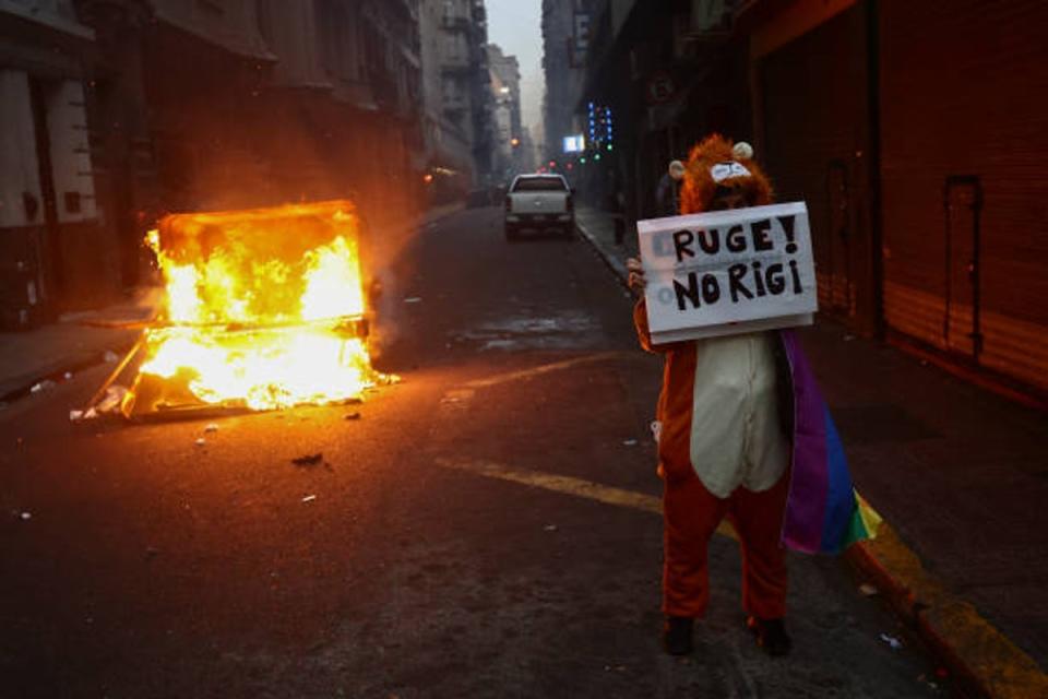 A demonstrator hold a sign against the new incentive regime for large investments included in President Milei’s reforms in front of a barricade on fire during a protest near the National Congress in Buenos Aires on 12 June 2024 (AFP via Getty Images)