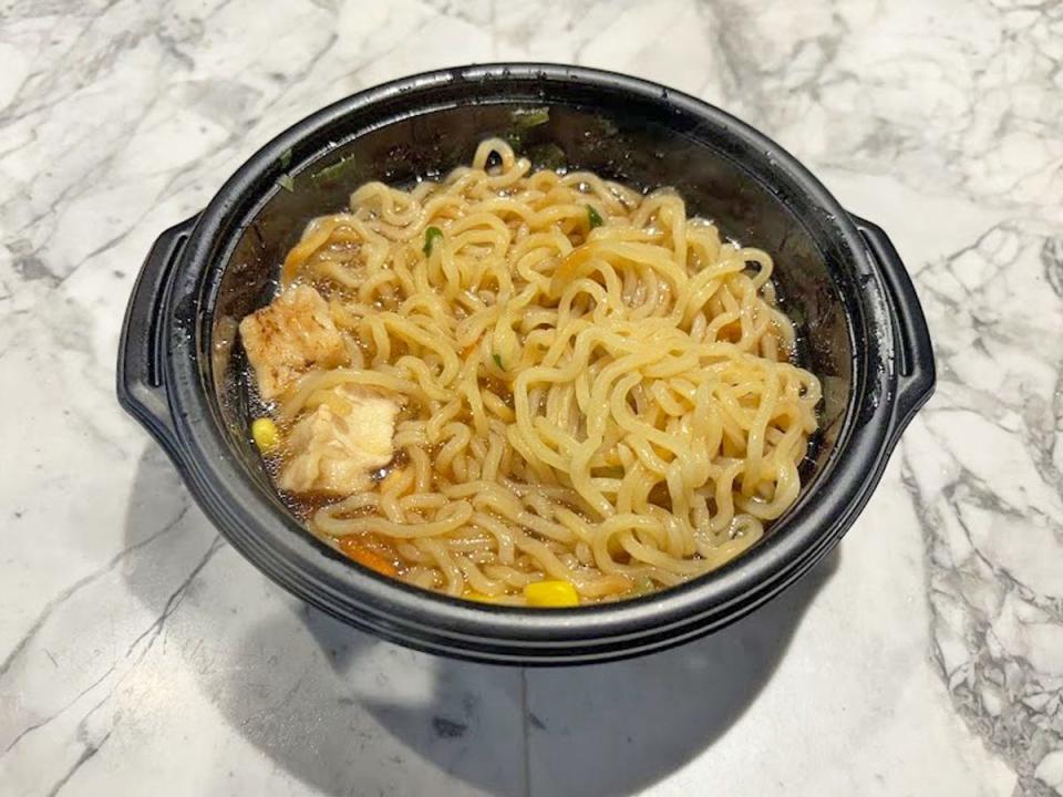 A black bowl of ramen noodles with a few pieces of chicken carrot, corn, and green onions mixed