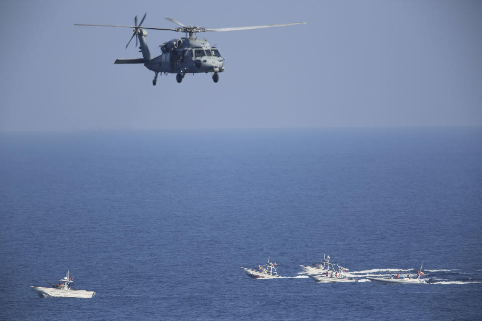 FILE - A U.S. MH-60 Seahawk helicopter flies over Iranian Revolutionary Guard patrol boats in the Strait of Hormuz on Dec. 21, 2018. The U.S. military is considering putting armed personnel on commercial ships traveling through the Strait of Hormuz, in what would be an unheard of action aimed at stopping Iran from seizing and harassing civilian vessels, four American officials told The Associated Press on Thursday, Aug. 3, 2023. (AP Photo/Jon Gambrell, File)