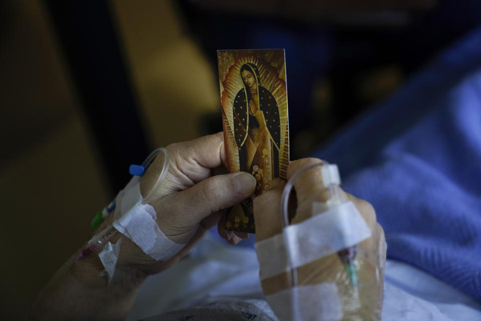 A patient holds an Our Lady of Guadalupe card in his bed while talking to chaplain Nancy Many at Providence Holy Cross Medical Center in the Mission Hills section of Los Angeles on Saturday, Jan. 9, 2021. As families are barred from visiting loved ones to curb the disease's spread, chaplains often are there to act as surrogates, holding the hands of the dying, praying with them and carrying iPads into hospital rooms to provide a real-time connection with grieving families. (AP Photo/Jae C. Hong)