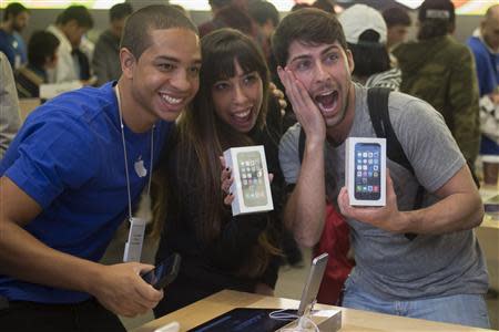 Alejandro de Rosa (R) and Melisa Racineti of Buenos Aires, Argentina pose with their new Apple iPhone 5s phones with Apple employee Jay at the Apple Retail Store on Fifth Avenue in Manhattan, New York September 20, 2013. Apple Inc's newest smartphone models hit stores on Friday in many countries across the world, including Australia and China. REUTERS/Adrees Latif