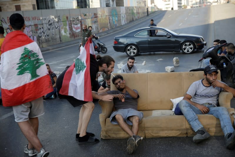 A demonstrator lights a cigarette to a fellow demonstrator as he sits on a sofa blocking a street during ongoing anti-government protests in Beirut