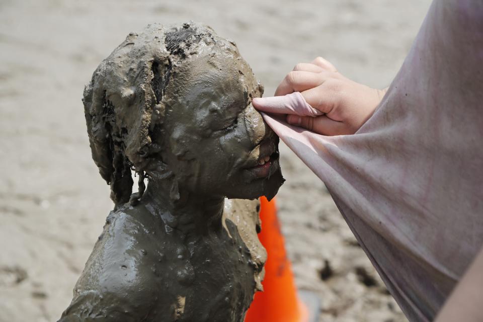 A participant in Mud Day gets her eyes wiped Tuesday, July 9, 2019, in Westland, Mich. The annual day sponsored by the Wayne County Parks takes place in a 75' x 150' giant mud pit that gives children the opportunity to get down and dirty at one of the messiest playgrounds Southeast Michigan has ever seen. (AP Photo/Carlos Osorio)