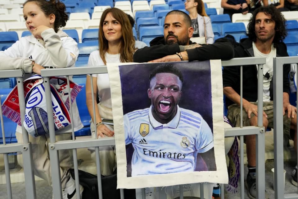 Spectators sit behind a photo of Real Madrid's Vinicius Junior prior to a Spanish La Liga soccer match between Real Madrid and Rayo Vallecano at the Santiago Bernabeu stadium in Madrid, Spain, Wednesday, May 24, 2023. (AP Photo/Manu Fernandez)