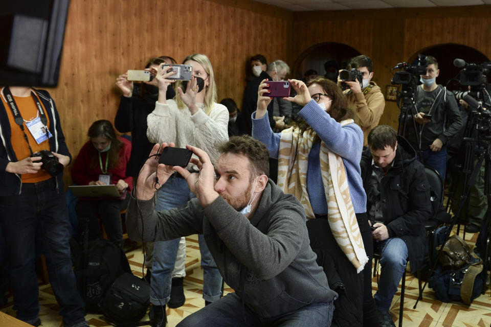 Journalists take pictures from a TV monitor showing Russian opposition leader Alexei Navalny speaking via a video link during a court session in Pokrov, Vladimir region, about 100 kilometers (62 miles) east of Moscow, Russia, Monday, Jan. 17, 2022. A new trial against Russian opposition leader Alexei Navalny has opened at the penal colony where he already is serving a prison term. Navalny is charged with fraud and contempt of court in the trial that opened on Tuesday, Feb. 15, 2022. (AP Photo/Denis Kaminev)