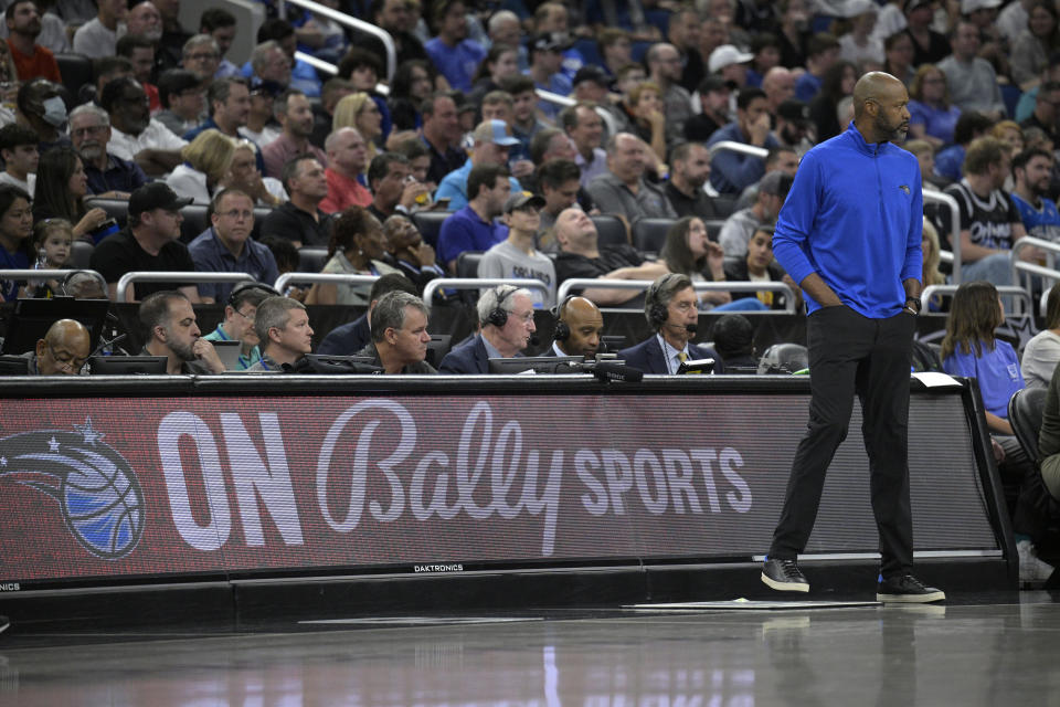 FILE - Orlando Magic coach Jamahl Mosley, right, stands next to an advertisement for Bally Sports during the first half of the team's NBA basketball game against the Detroit Pistons, Feb. 23, 2023, in Orlando, Fla. Diamond Sports Group, the largest owner of regional sports networks, filed for Chapter 11 bankruptcy protection Tuesday, March 14. The move came after it missed a $140 million interest payment last month. Diamond owns 19 networks under the Bally Sports banner. Those networks have the rights to 42 professional teams — 14 baseball, 16 NBA and 12 NHL. (AP Photo/Phelan M. Ebenhack, File)