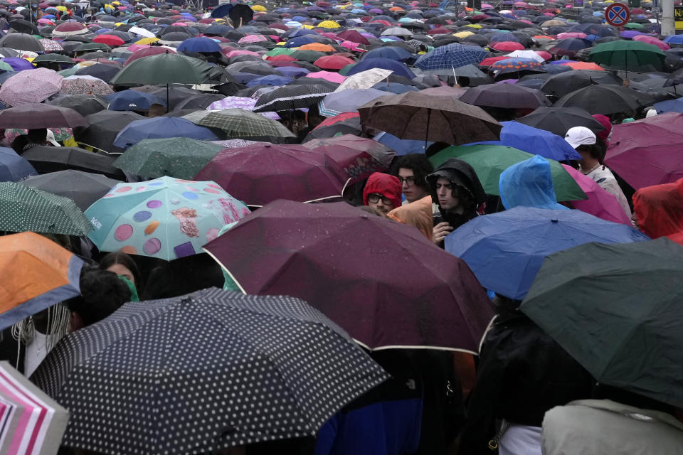 People take shelter from the rain during a free concert organized by the main Italian Labour Unions on May Day in St. John in Lateran Square in Rome, Monday, May 1, 2023. (AP Photo/Alessandra Tarantino)