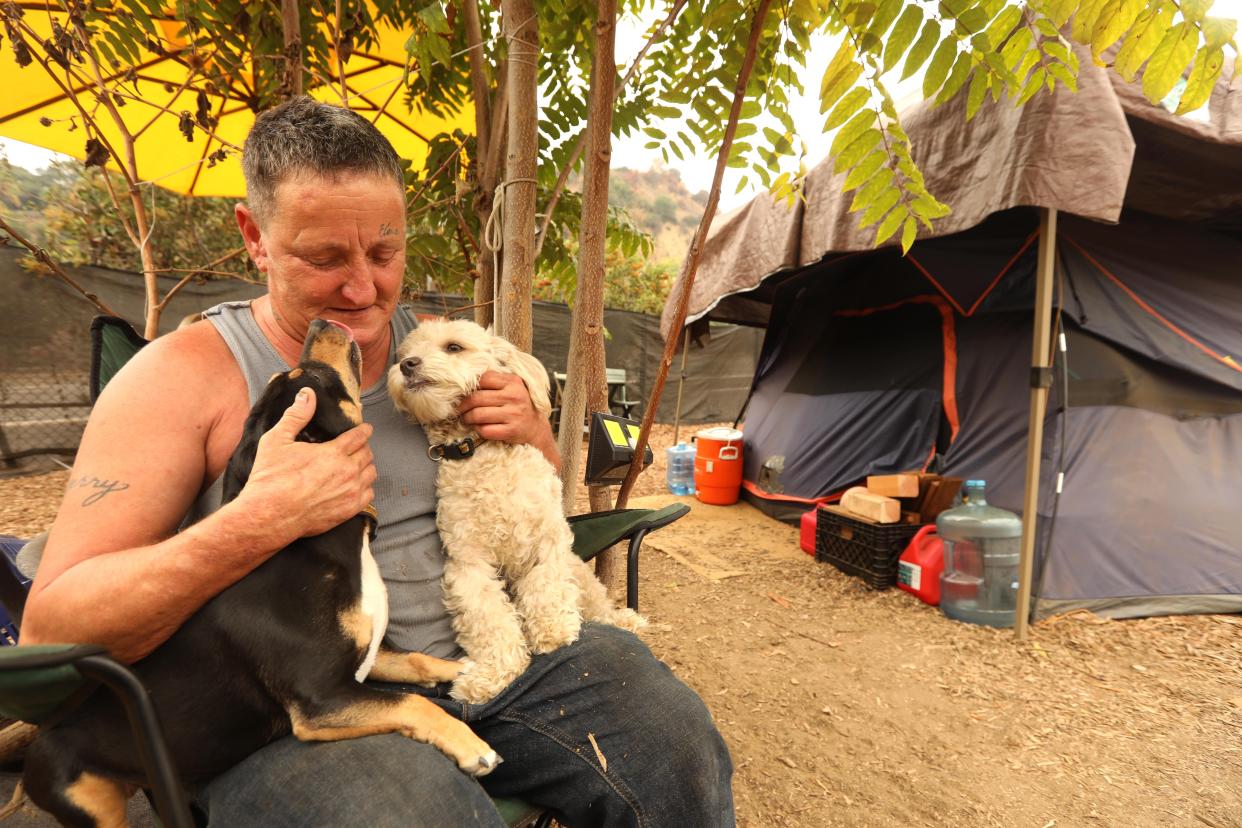A woman sits with two small dogs on her lap outside a tent.