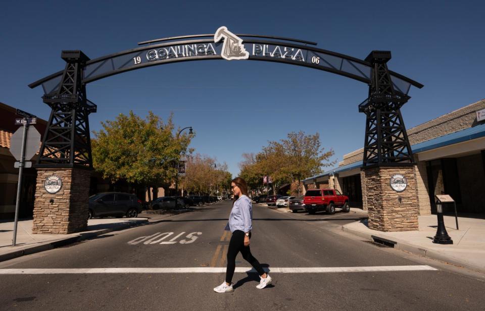 Argelia Leon walks across the street of Coalinga Plaza under an arch with a pumpjack motif.