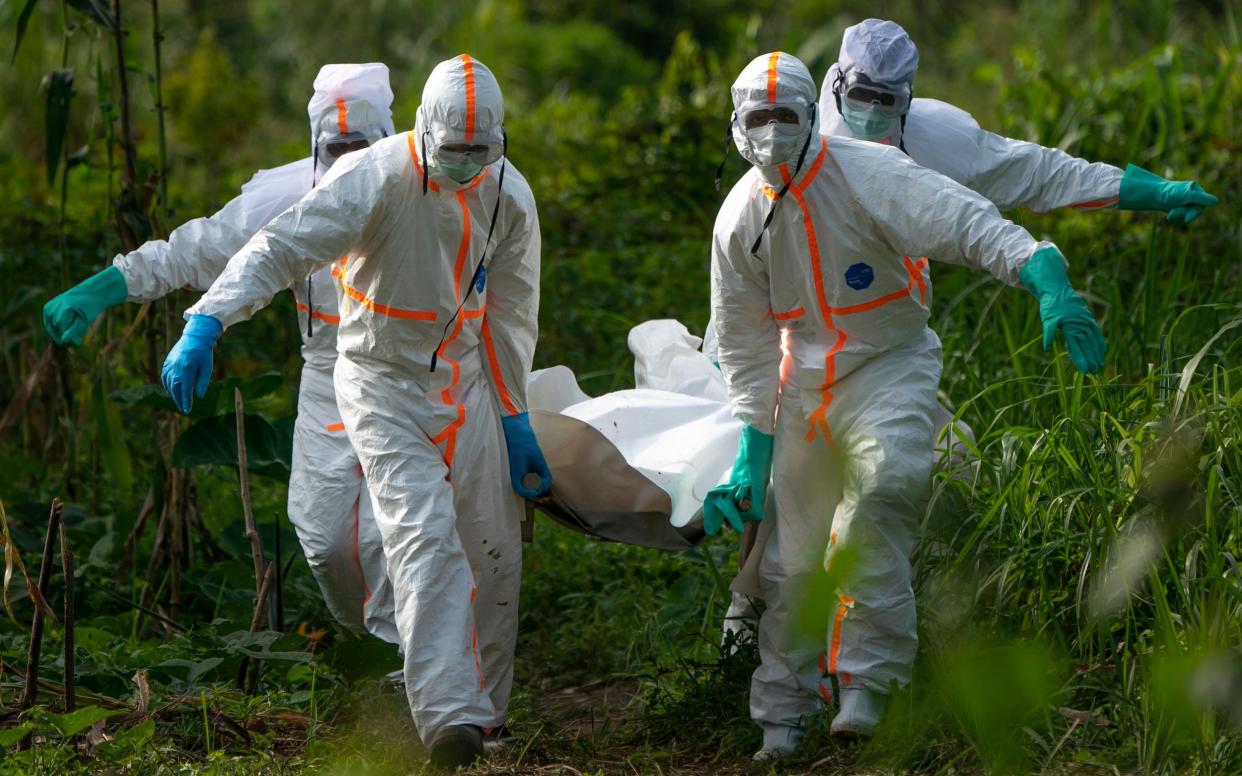 Burial workers in the Congo, dressed in protective gear, carry the remains of an Ebola victim  - AP
