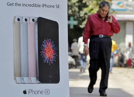 FILE PHOTO: A man speaks on his mobile phone as he walks past an Apple iPhone advertisement billboard on a street in New Delhi, India, April 25, 2016. REUTERS/Anindito Mukherjee/File Photo