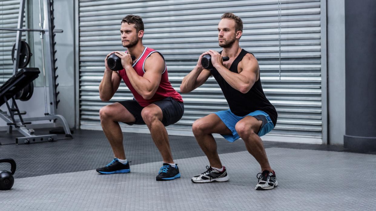  Two men squatting with a kettlebell using goblet hold during workout. 