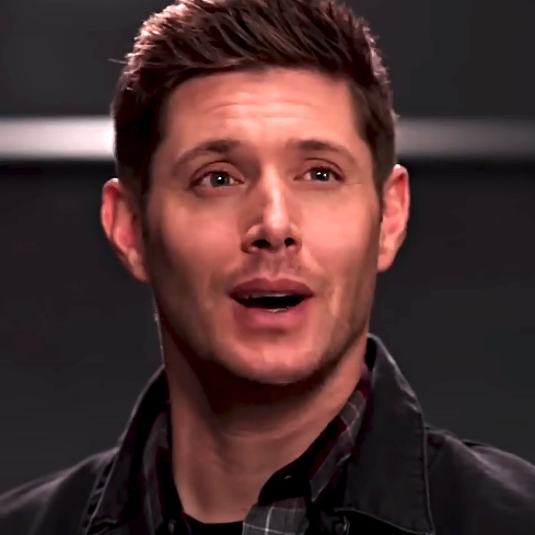 Jensen Ackles smiles in a checkered shirt under a jacket, short hair, indoors