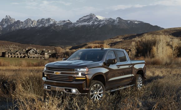 A 2019 Chevrolet Silverado High Country pickup truck in a field, with mountains and a building in the background.