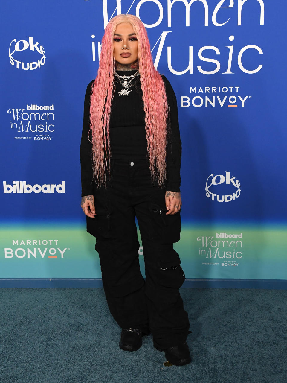 she's posing in baggy cargo pants and long sleeved shirt with long pink hair  and silver jewelry