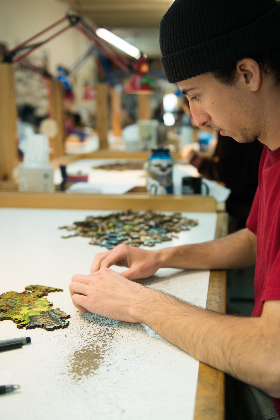 A man in a red shirt works with puzzle pieces on a white table.