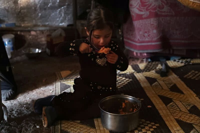 An internally displaced girl eats inside a tent at a makeshift camp in Azaz