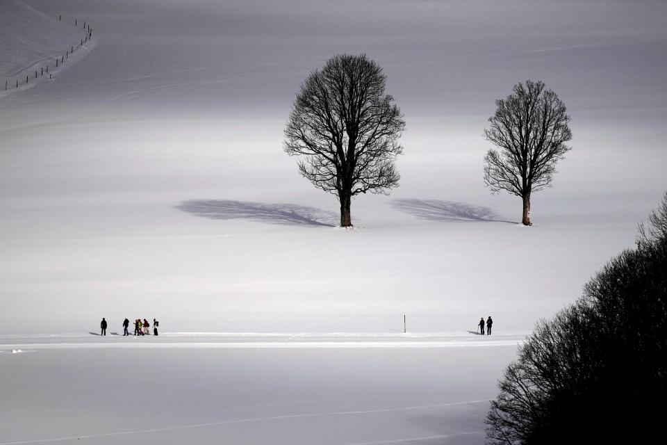 People walk through a snow covered landscape in Ramsau, Austria, Saturday, Dec.16, 2023. (AP Photo/Matthias Schrader)