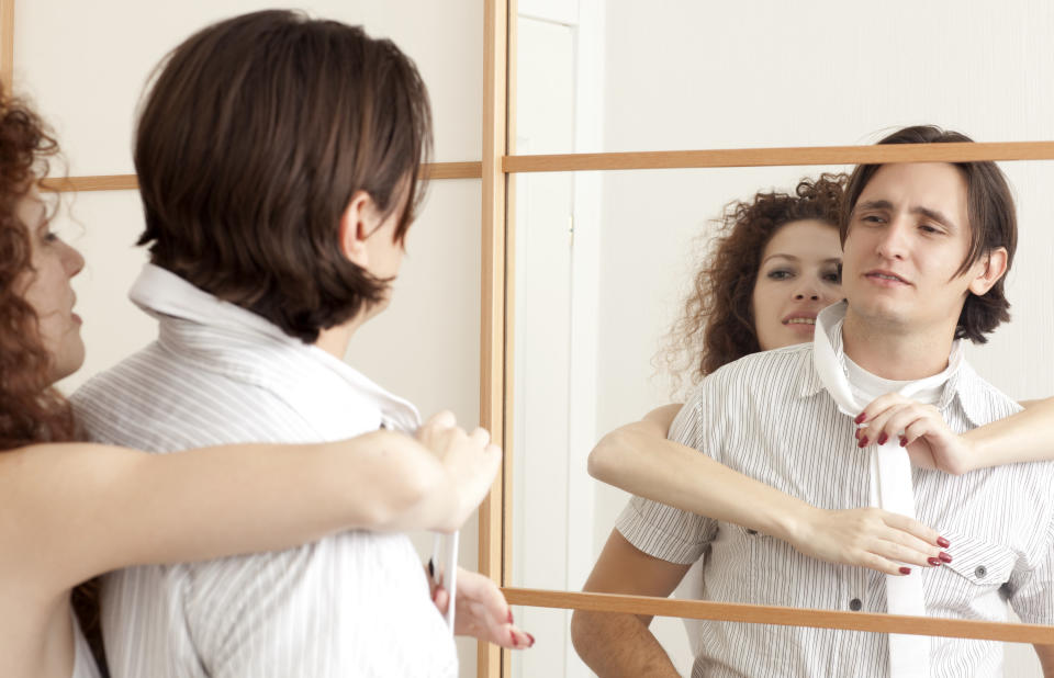 Young woman assistance her boyfriend tying a tie. They looking at cupboard mirror