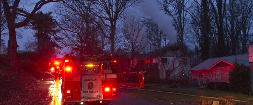 Asheville, North Carolina, USA - February 16, 2016:  A firetruck lights up the night parked on a street next to a house on fire with smoke coming out of it