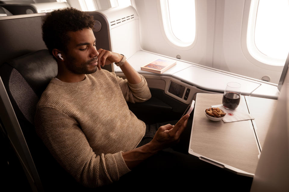 A man using Air Pods relaxing and enjoying a glass of red wine and snack in Air Canada Business Class