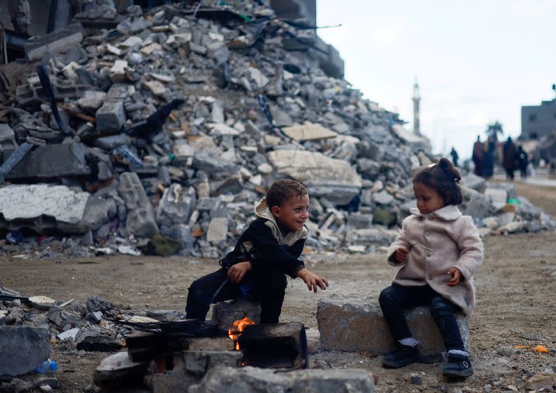 Niños palestinos sentados junto al fuego junto a los escombros de una casa alcanzada por un ataque israelí, en Jan Yunis