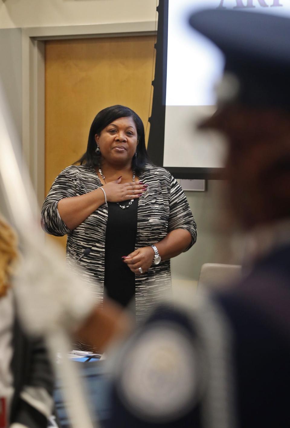 Akron Public Schools Superintendent Christine Fowler Mack recites the Pledge of Allegiance at a school board meeting as a member of the Buchtel JROTC Air Force color guard holds a flag.