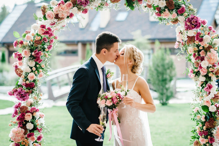 A bride and groom kissing and posing under a flower archway.