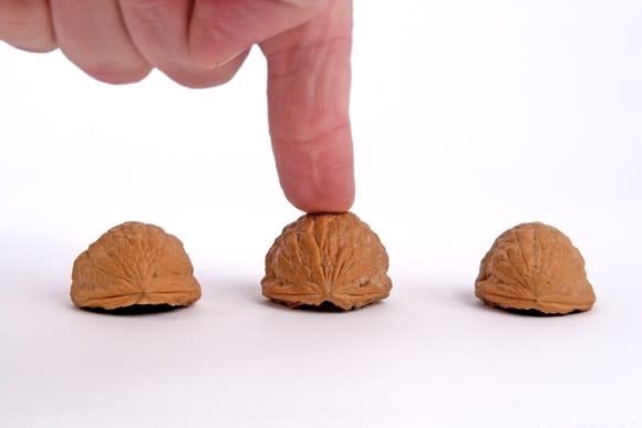 Finger on middle shell of three shells that are part of a shell game