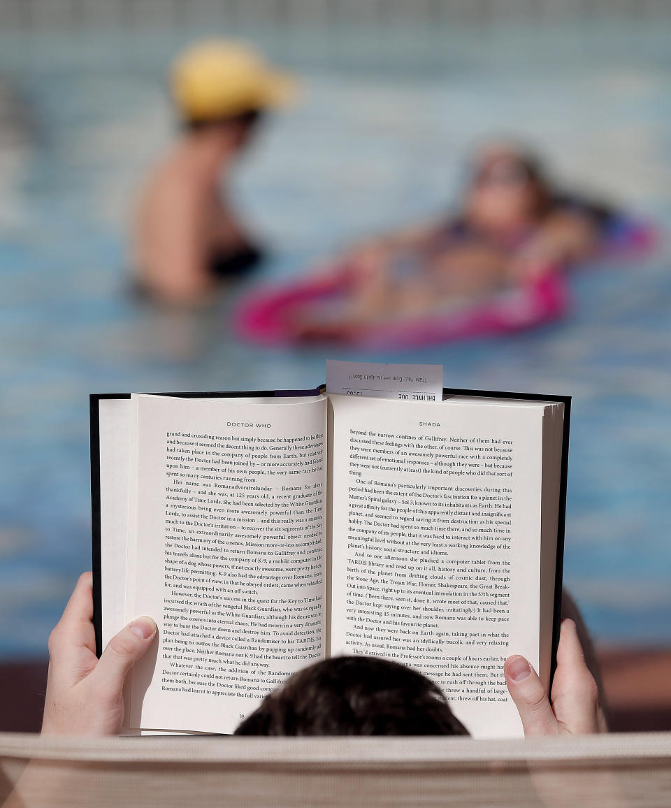 Robert Wasik, of Minnesota, reads "Dr. Who" poolside as guest float in the pool at the Mission Palms, Friday, Feb. 14, 2014 in Tempe, Ariz. With large parts of the country in the grips of frigid cold and snow and ice storms, the Southwest is enjoying a heat wave that is setting record highs and sending people to pools, golf courses and beaches in large numbers. Phoenix and Los Angeles are experiencing unusually warm 80-degree weather that has residents and visitors rejoicing as they look at the mess on the East Coast.(AP Photo/Matt York)