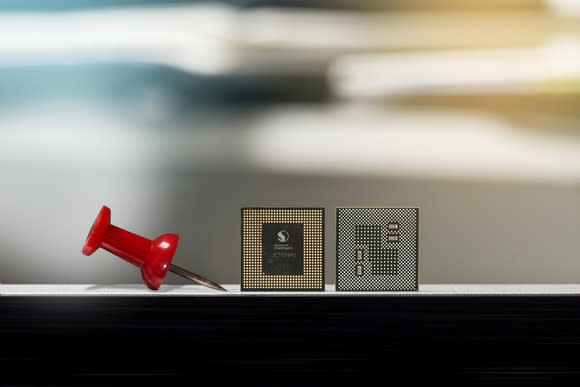From left to right: a pushpin, a Snapdragon processor facing toward the camera, and a Snapdragon processor facing away from the camera