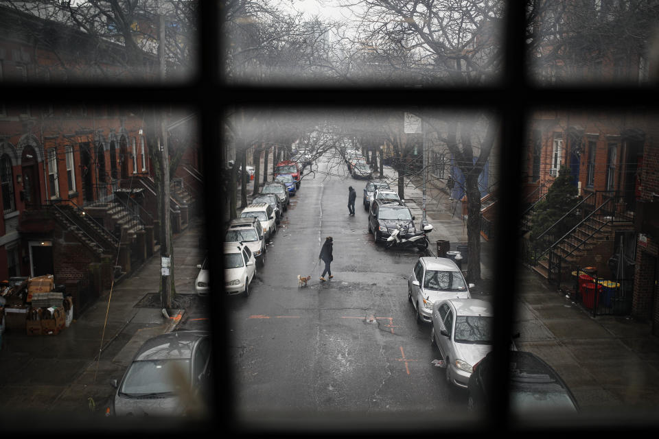 A pedestrian walks their dog through a quiet street, Tuesday, March 17, 2020, in the Brooklyn borough of New York. As of Sunday, nearly 2,000 people with the virus have been hospitalized in the state of New York, and 114 have died, officials said. More than 15,000 have tested positive statewide, including 9,000 in New York City. (AP Photo/John Minchillo)