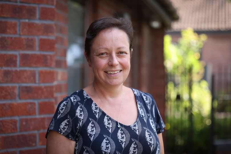 Framework's deputy chief executive Claire McGonigle, pictured in front of a red brick building wearing a blue top patterned with white leaf shapes