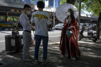 A woman wearing a face mask and holding a parasol stands along a street in the central business district in Beijing, Thursday, July 7, 2022. (AP Photo/Mark Schiefelbein)