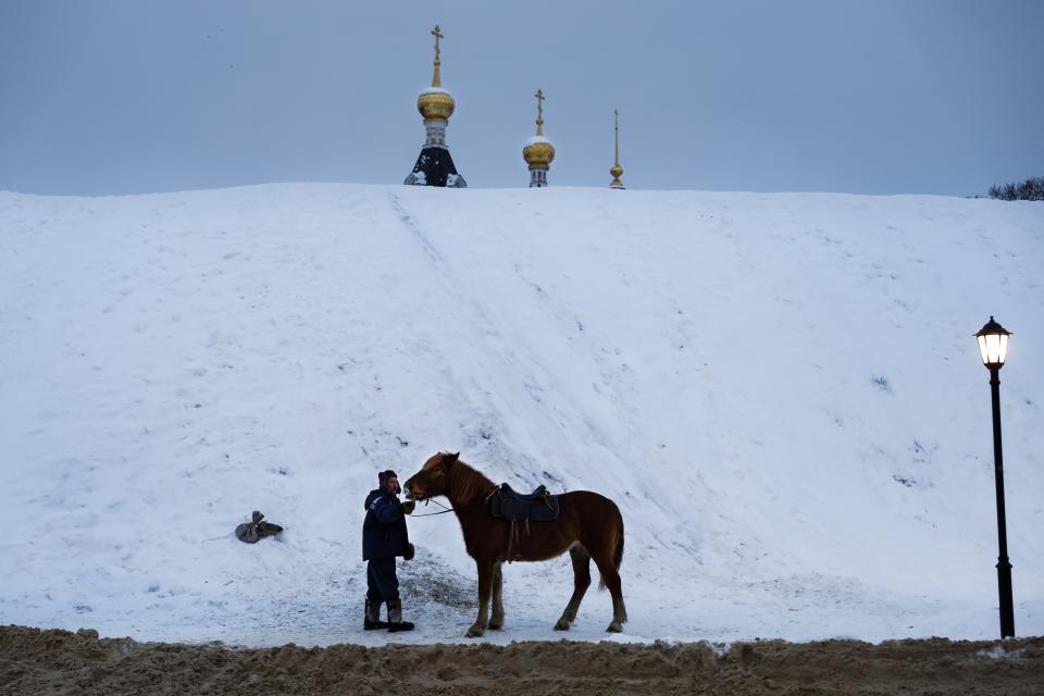 A man prepares a horse to ride tourists during a cold winter day at a hill, near the Assumption Cathedral built in XVI century in the background, in the small Russian town of Dmitrov, about 75 kilometers (47 miles) north from Moscow, Russia, Saturday, Jan. 12, 2019. Temperatures dipped to -10 C (14 F) in Moscow and -13 C (9 F) at night. (AP Photo/Alexander Zemlianichenko)