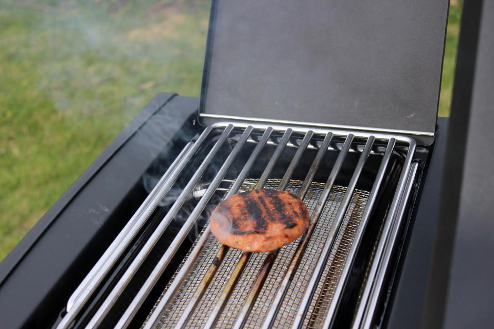 A close up of a burger smoking on the side burner of the Napoleon Phantom Rogue SE 425 RSIB