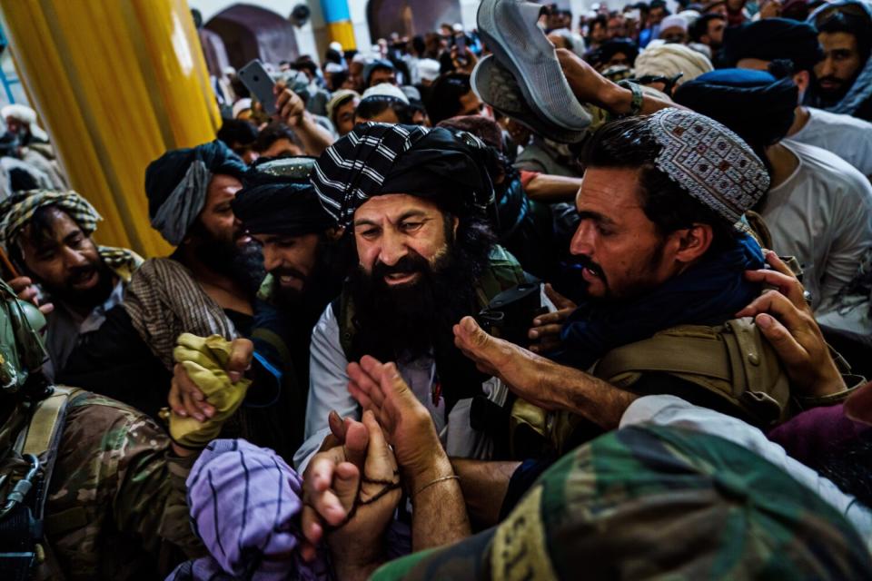 Hands reach out from a swarm of people surrounding a bearded smiling man moving through the crowd.