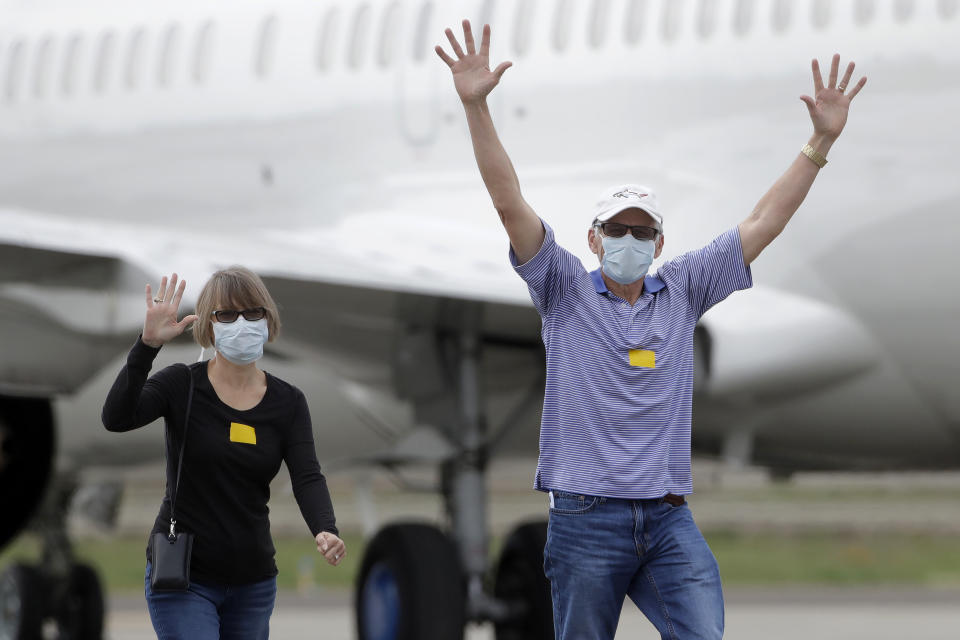 FILE - In this March 10, 2020, file photo, passengers from the Grand Princess, a cruise ship carrying multiple people who have tested positive for COVID-19, gesture toward reporters while walking on a tarmac before boarding a chartered plane in Oakland, Calif., on March 10, 2020. The passengers on the flight were going to San Antonio to be quarantined at Lackland Air Force Base. A year ago, the Grand Princess captured the world’s attention when it became clear the coronavirus pandemic had arrived on the shore of California, making the virus real to millions in the United States. Now, some of those who traveled on the ship on trips to Mexico and Hawaii are reliving the pain that followed after losing loved ones infected with the coronavirus aboard the ship. (AP Photo/Jeff Chiu, File)