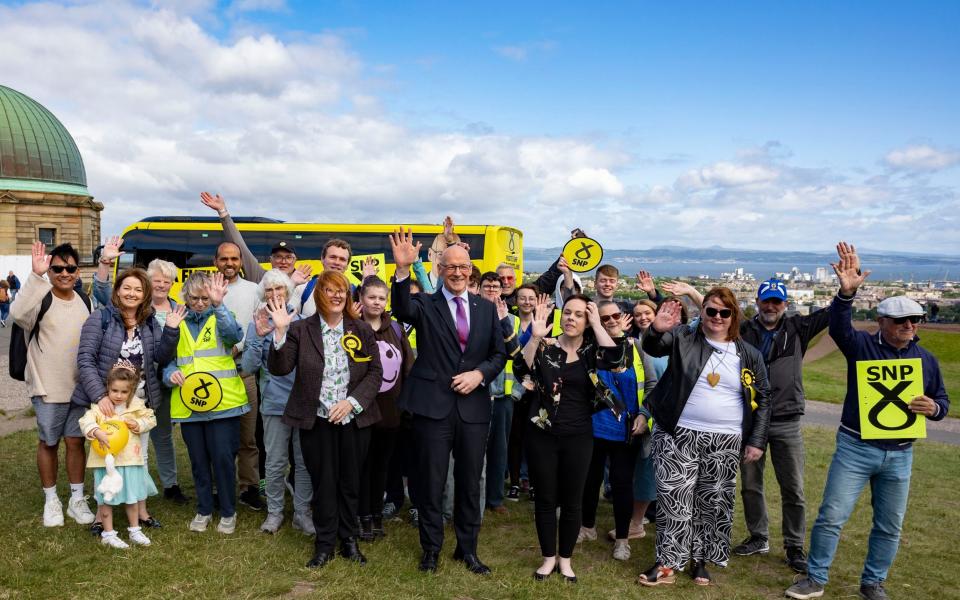 John Swinney and Kate Forbes stand with a crowd of SNP supporters on a hilltop above Dundee, with the Firth of Tay and Fife seen behind them