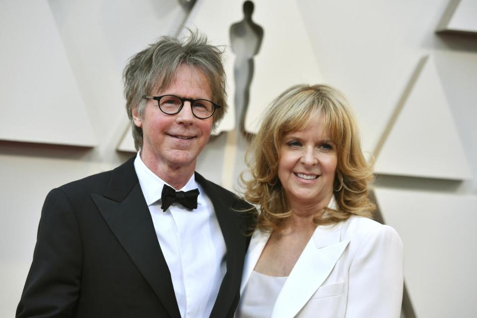 Dana Carvey wears a black and white suit and smiles and poses next to Paula Zwagerman, who is in a white suit.