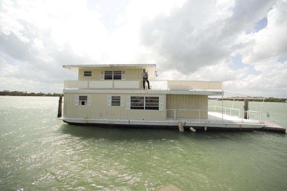 In this April 22, 2014 photo, Fane Lozman poses for photos holding his dog on his home floating in the waters near North Bay Village, Fla. Lozman caught legal lightning in a bottle last year when the U.S. Supreme Court agreed with him that his floating home was a house, not a vessel covered by maritime law. But the justices haven’t had the last word: Lozman is still fighting for compensation for the home, which was destroyed years ago. The Fort Lauderdale-based federal judge whose decision on the floating home was overturned, U.S. District Judge William Dimitrouleas, refused earlier this year to give Lozman any of the $25,000 bond posted by the city of Riviera Beach to pay for Lozman’s home in case he won. (AP Photo/J Pat Carter)