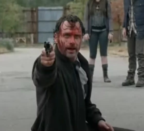 Andrew Lincoln as Rick Grimes covered in blood pointing his gun at someone