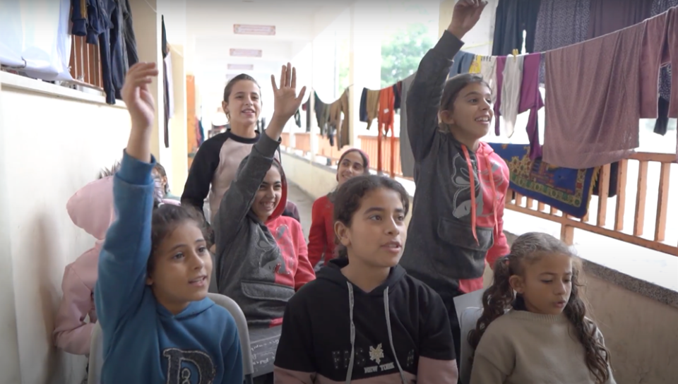 Estudiantes escuchando al profesor, algunos levantando la mano.