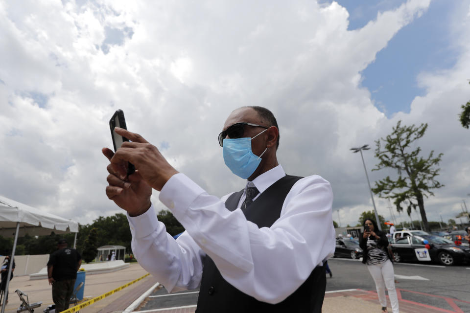 Eugene Picquet, father of graduate Jeremiah Fred, takes photos while wearing a mask as the New Orleans Charter Science and Math High School class of 2020 holds a drive-in graduation ceremony as a result of the COVID-19 pandemic, outside Delgado Community College in New Orleans, Wednesday, May 27, 2020. Students and family got out of their cars to receive diplomas one by one, and then held a parade of cars through city streets. (AP Photo/Gerald Herbert)